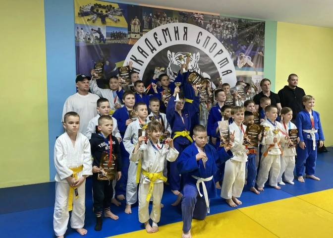Ученики академии с кубками и грамотами на фоне эмблемы «Академия спорта»